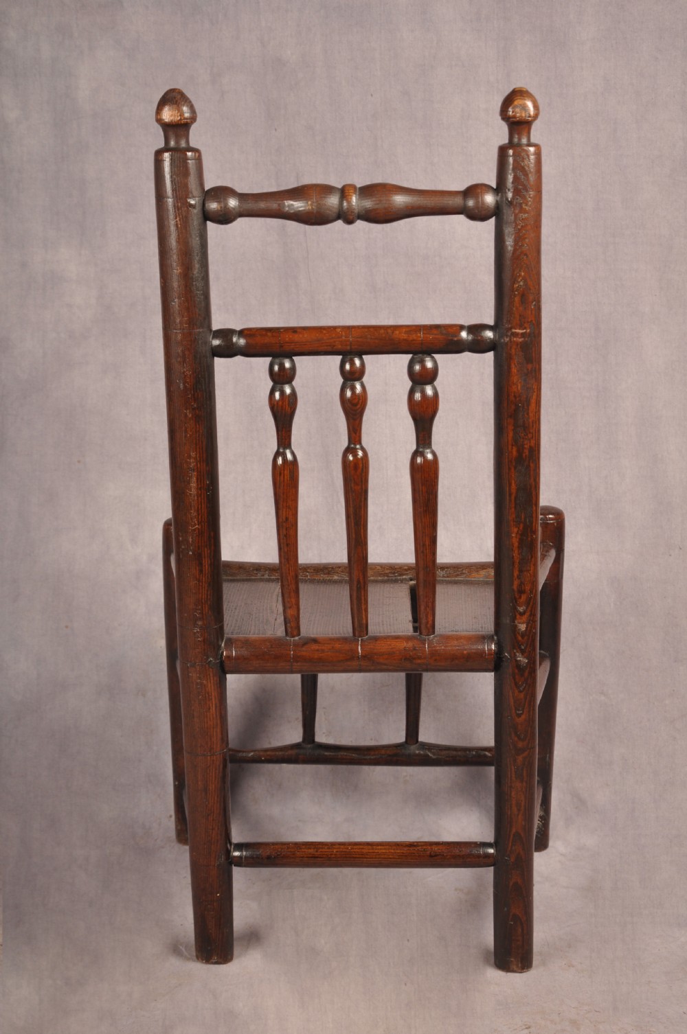 A near pair of dark 17th-century turned ash chairs with spindle backrests, turned stretchers, panel seats, and top finials. View X