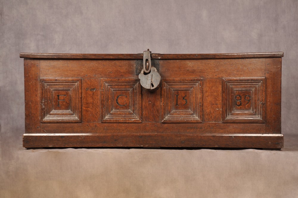 A dark oak Elizabethan coffer featuring four carved recessed panels inscribed with initials and the year 1589, secured with a central iron lock.