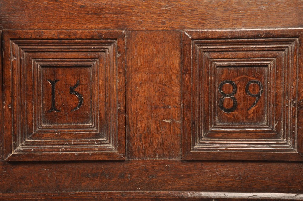 A dark oak Elizabethan coffer featuring four carved recessed panels inscribed with initials and the year 1589, secured with a central iron lock. View II