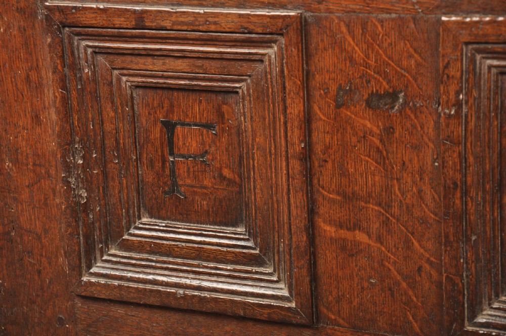 A dark oak Elizabethan coffer featuring four carved recessed panels inscribed with initials and the year 1589, secured with a central iron lock. View IV