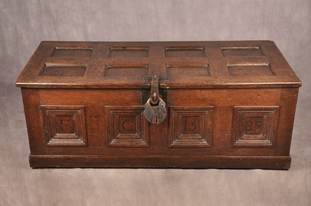 A dark oak Elizabethan coffer featuring four carved recessed panels inscribed with initials and the year 1589, secured with a central iron lock. View V
