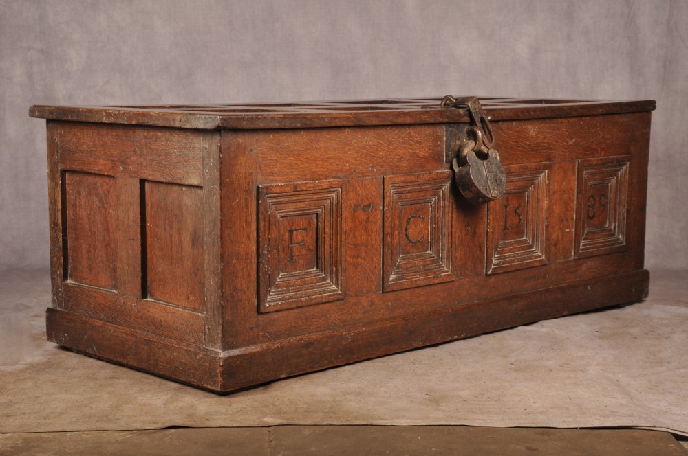 A dark oak Elizabethan coffer featuring four carved recessed panels inscribed with initials and the year 1589, secured with a central iron lock. View VII