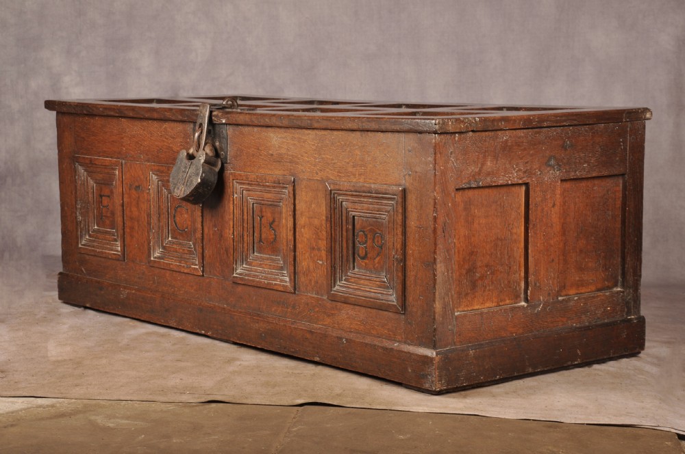 A dark oak Elizabethan coffer featuring four carved recessed panels inscribed with initials and the year 1589, secured with a central iron lock. View VIII