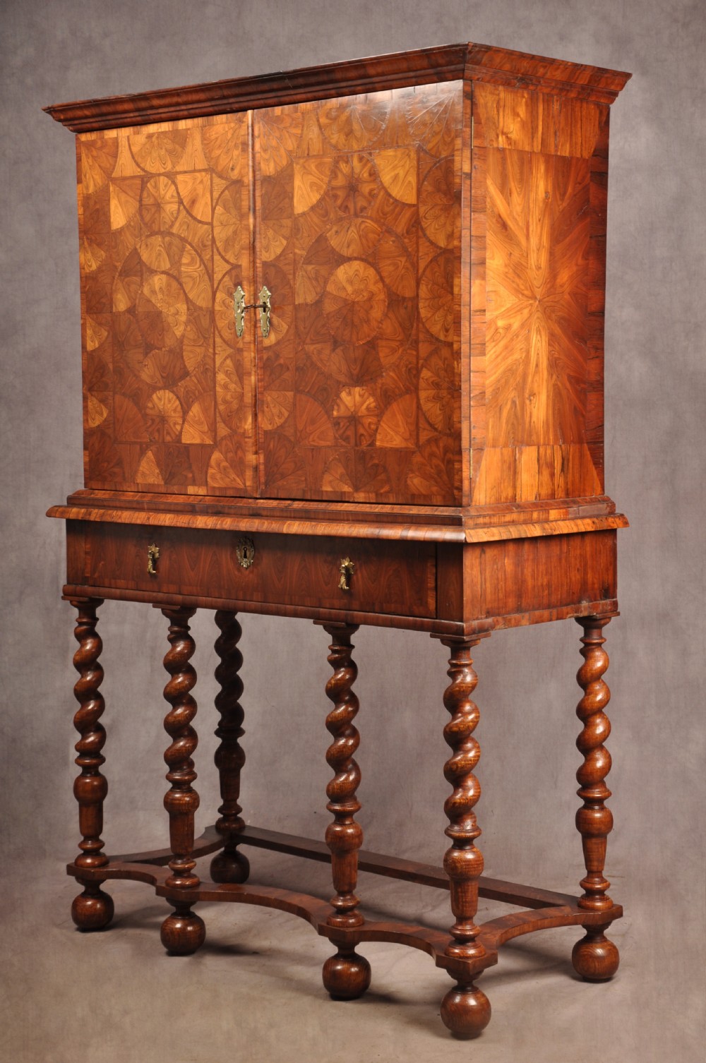 A seventeenth-century kingwood cabinet on stand featuring geometric oyster parquetry doors, a single frieze drawer, six barley twist legs, and a shaped stretcher.