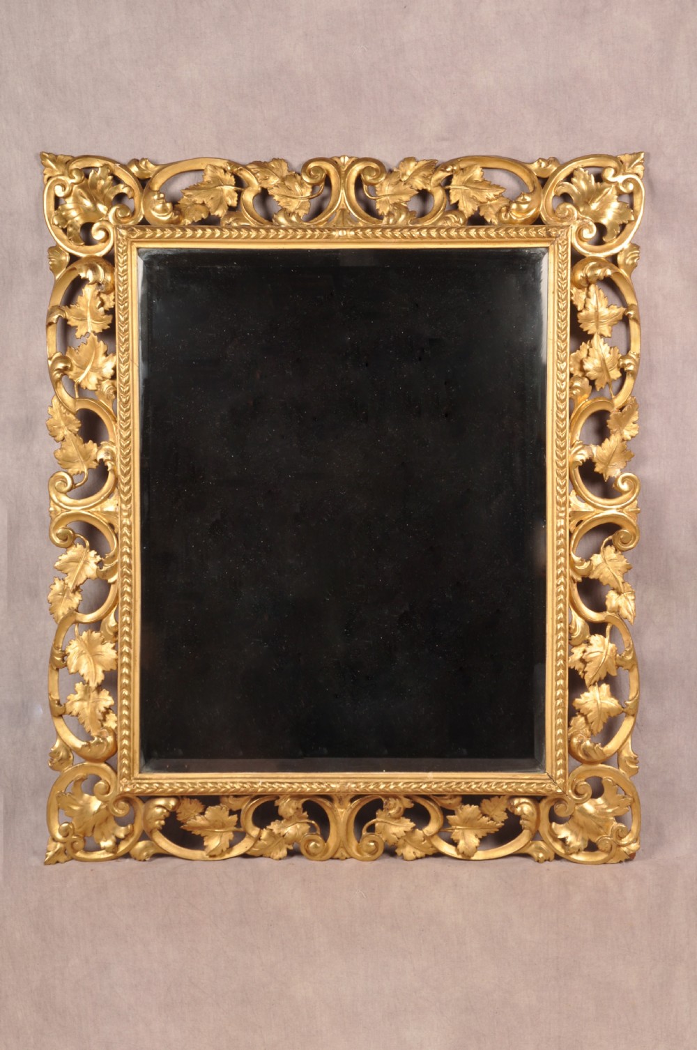 An early nineteenth-century rectangular wall mirror set within a deeply carved Florentine giltwood frame featuring openwork foliage, scrolls, and a beaded inner edge.