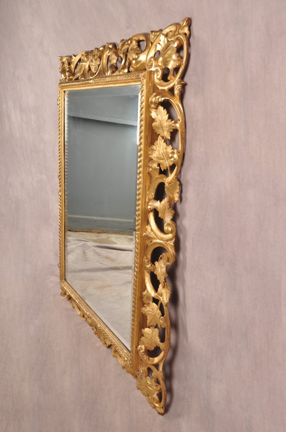 An early nineteenth-century rectangular wall mirror set within a deeply carved Florentine giltwood frame featuring openwork foliage, scrolls, and a beaded inner edge. View VI