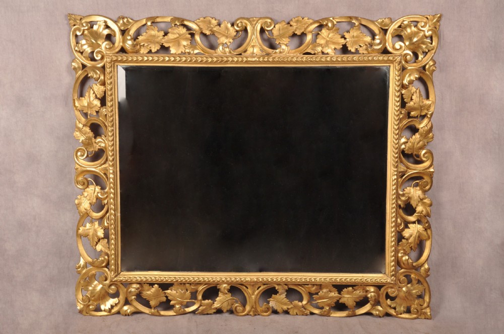 An early nineteenth-century rectangular wall mirror set within a deeply carved Florentine giltwood frame featuring openwork foliage, scrolls, and a beaded inner edge. View VII