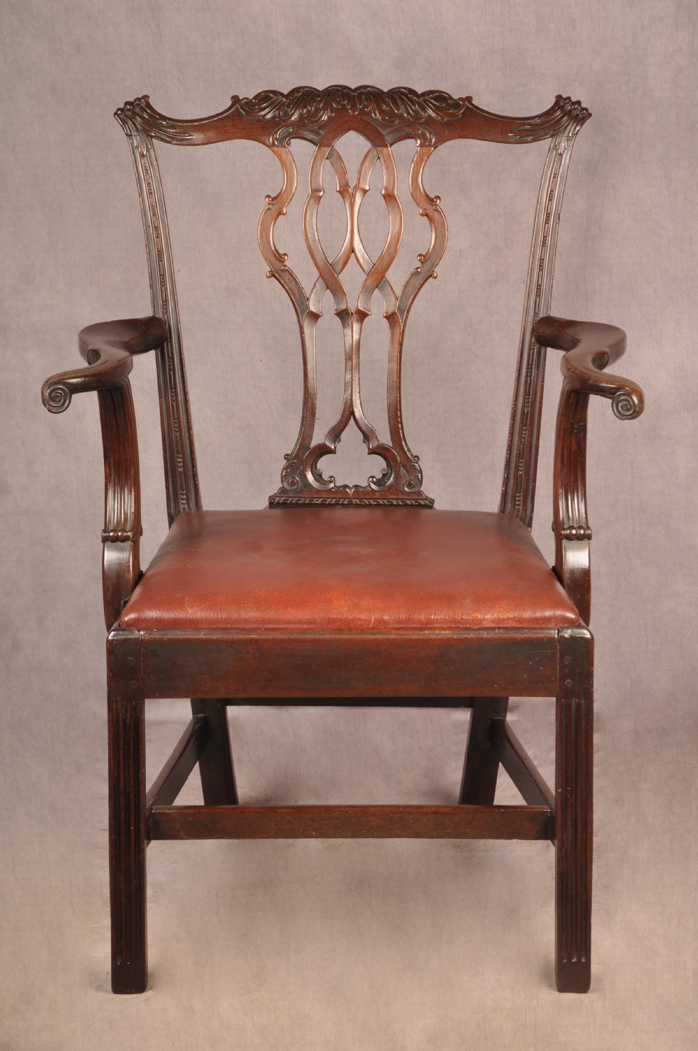 An 18th-century Chippendale mahogany armchair featuring an intricately carved Gothic tracery back splat, out-swept armrests, a brown leather seat, and square legs.