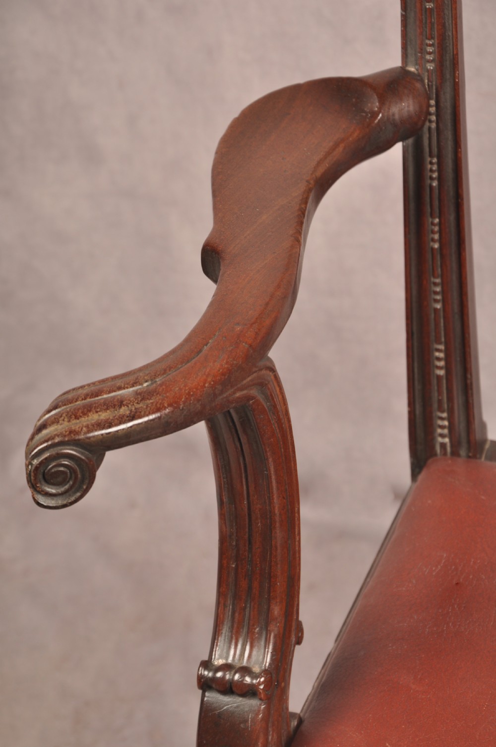 An 18th-century Chippendale mahogany armchair featuring an intricately carved Gothic tracery back splat, out-swept armrests, a brown leather seat, and square legs. View V