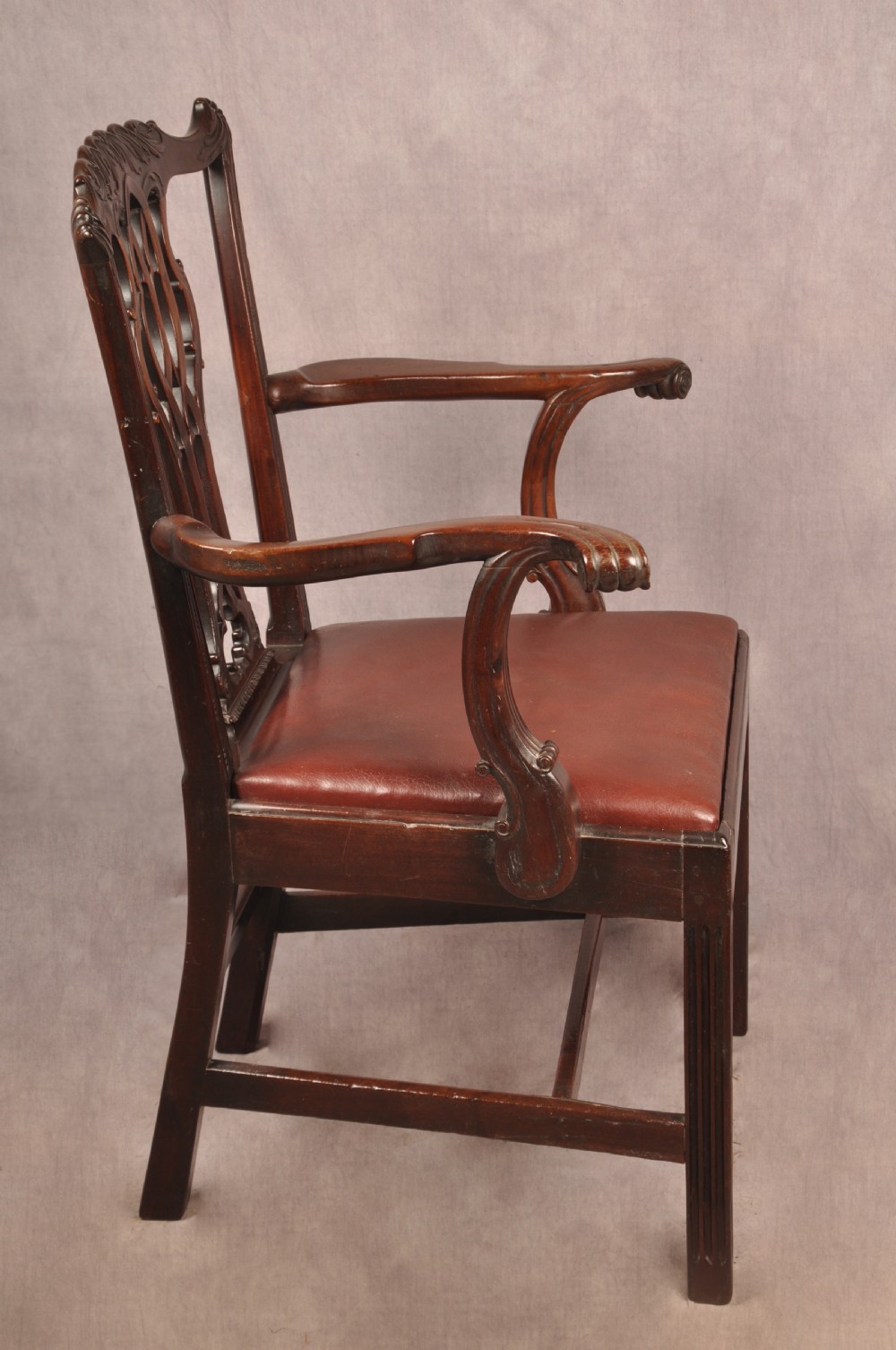 An 18th-century Chippendale mahogany armchair featuring an intricately carved Gothic tracery back splat, out-swept armrests, a brown leather seat, and square legs. View XIII