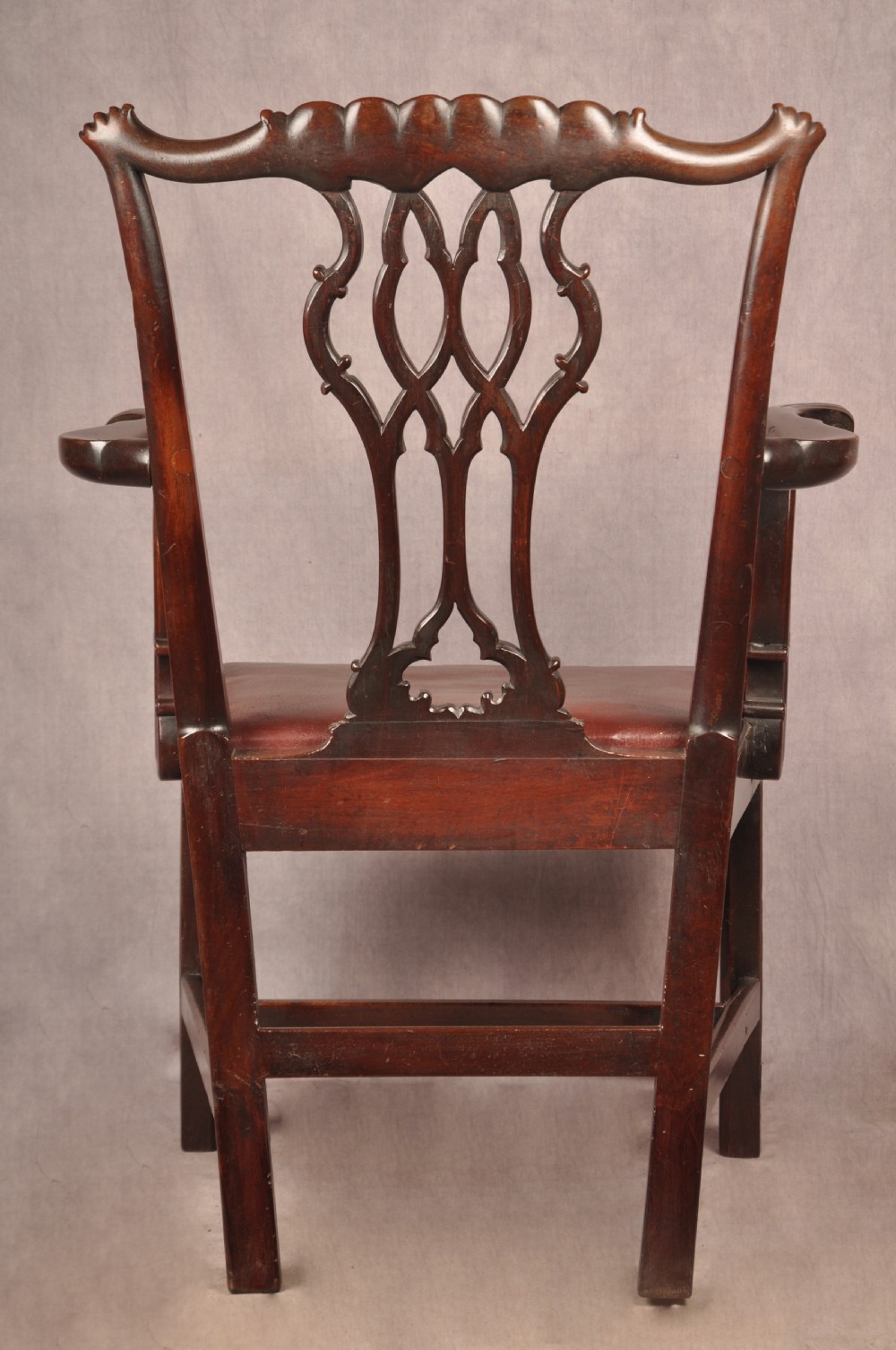 An 18th-century Chippendale mahogany armchair featuring an intricately carved Gothic tracery back splat, out-swept armrests, a brown leather seat, and square legs. View XIV