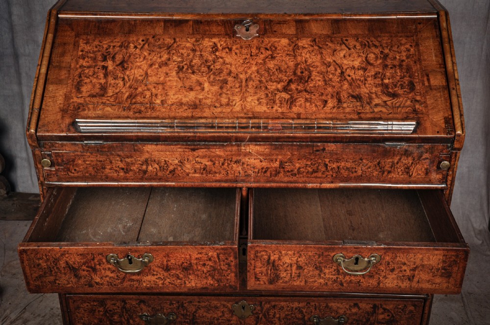 A late 17th-century slant-front bureau featuring highly figured mulberry veneer, brass drop handles, keyhole escutcheons, and four drawers resting on bracket feet. View XII