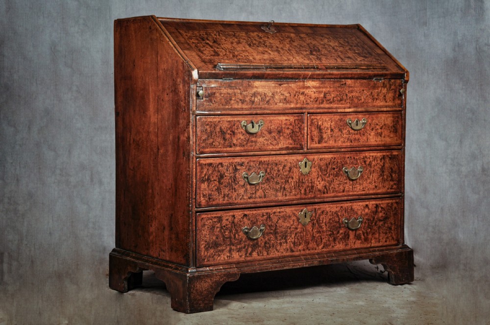 A late 17th-century slant-front bureau featuring highly figured mulberry veneer, brass drop handles, keyhole escutcheons, and four drawers resting on bracket feet. View XIII