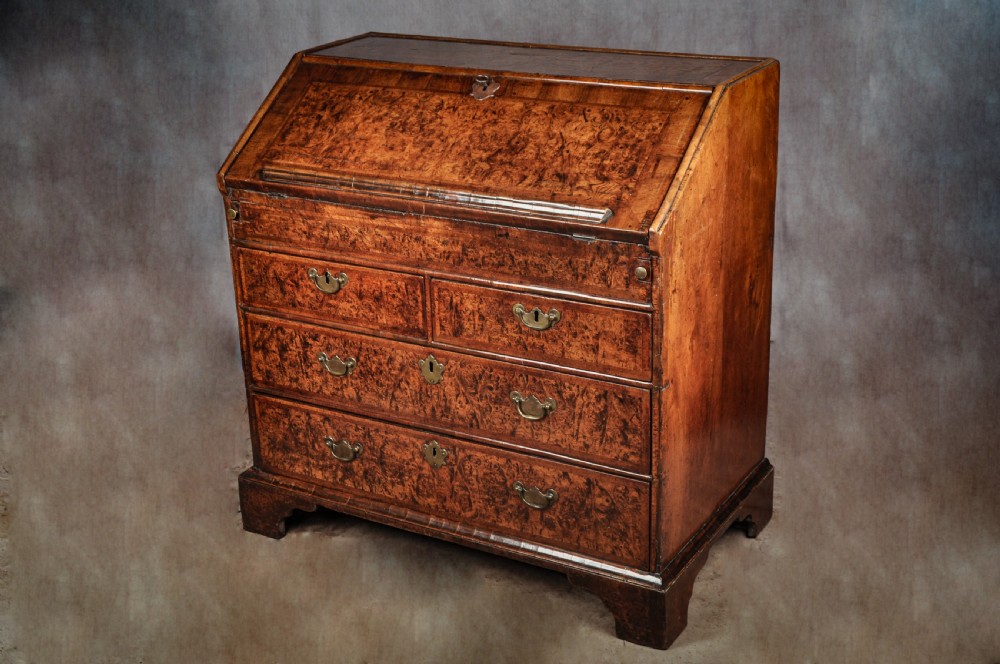 A late 17th-century slant-front bureau featuring highly figured mulberry veneer, brass drop handles, keyhole escutcheons, and four drawers resting on bracket feet. View XIV