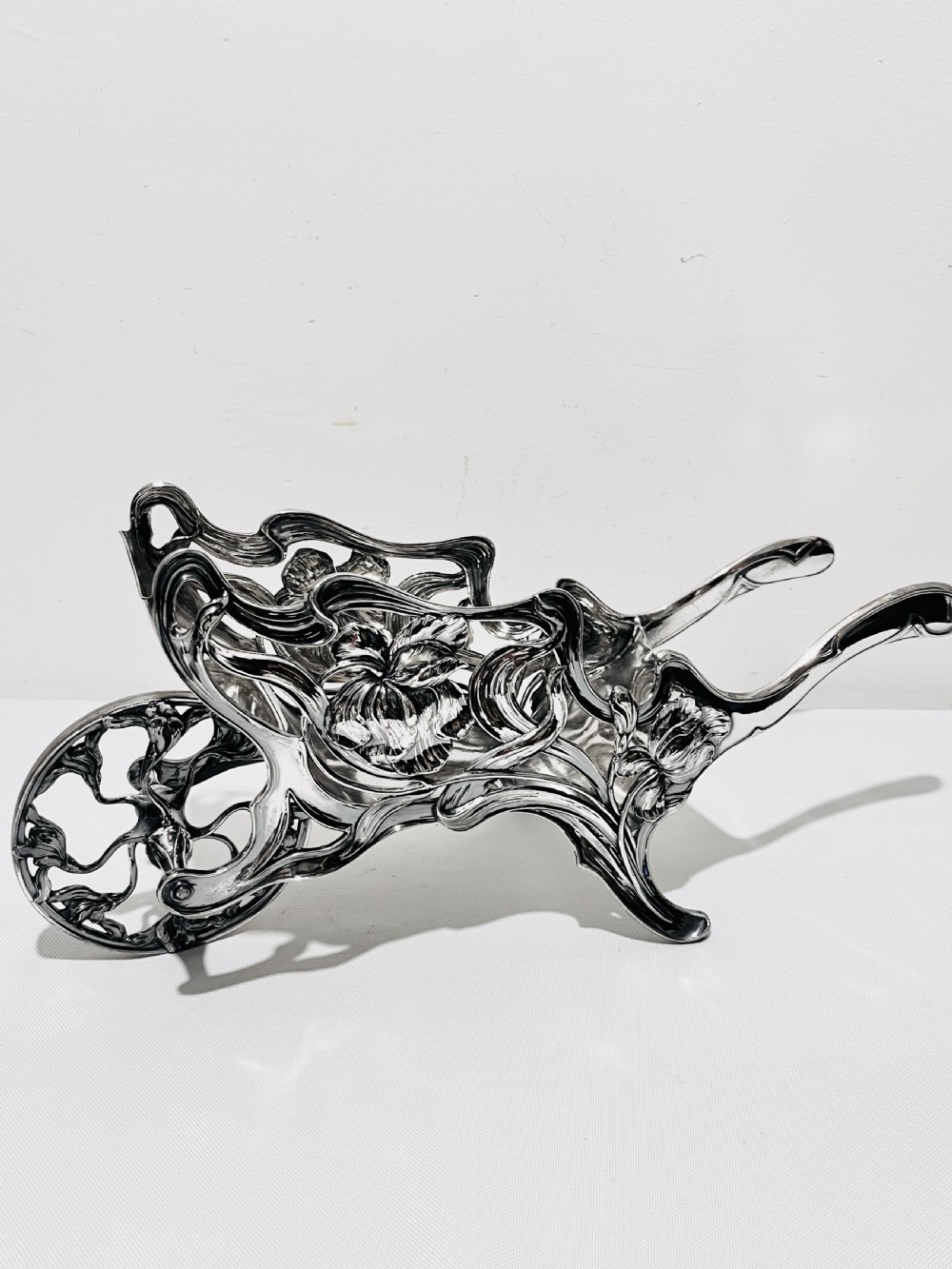 An Art Nouveau silver-plated wine wagon shaped like a stylized wheelbarrow with intricate botanical openwork and flowing organic curves.