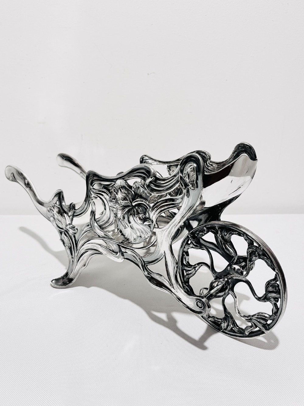 An Art Nouveau silver-plated wine wagon shaped like a stylized wheelbarrow with intricate botanical openwork and flowing organic curves. View VI