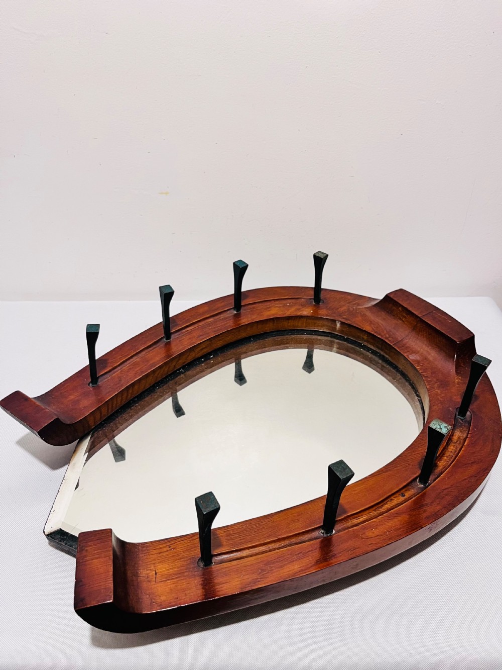 A Victorian horseshoe-shaped wooden wall mirror with bevelled glass and dark metal nail pegs along the frame.