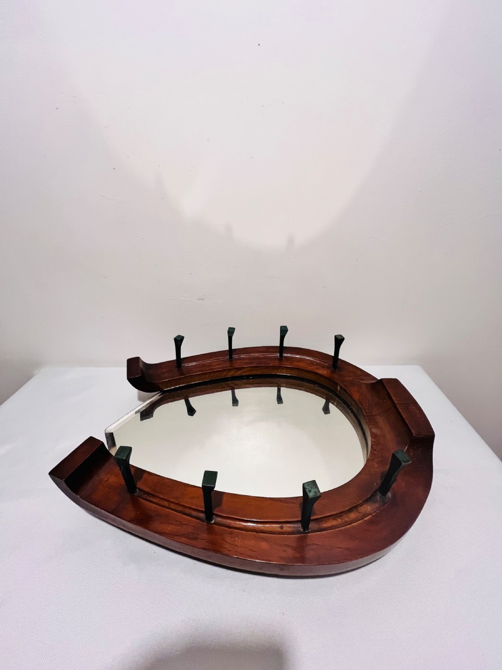 A Victorian horseshoe-shaped wooden wall mirror with bevelled glass and dark metal nail pegs along the frame. View IV