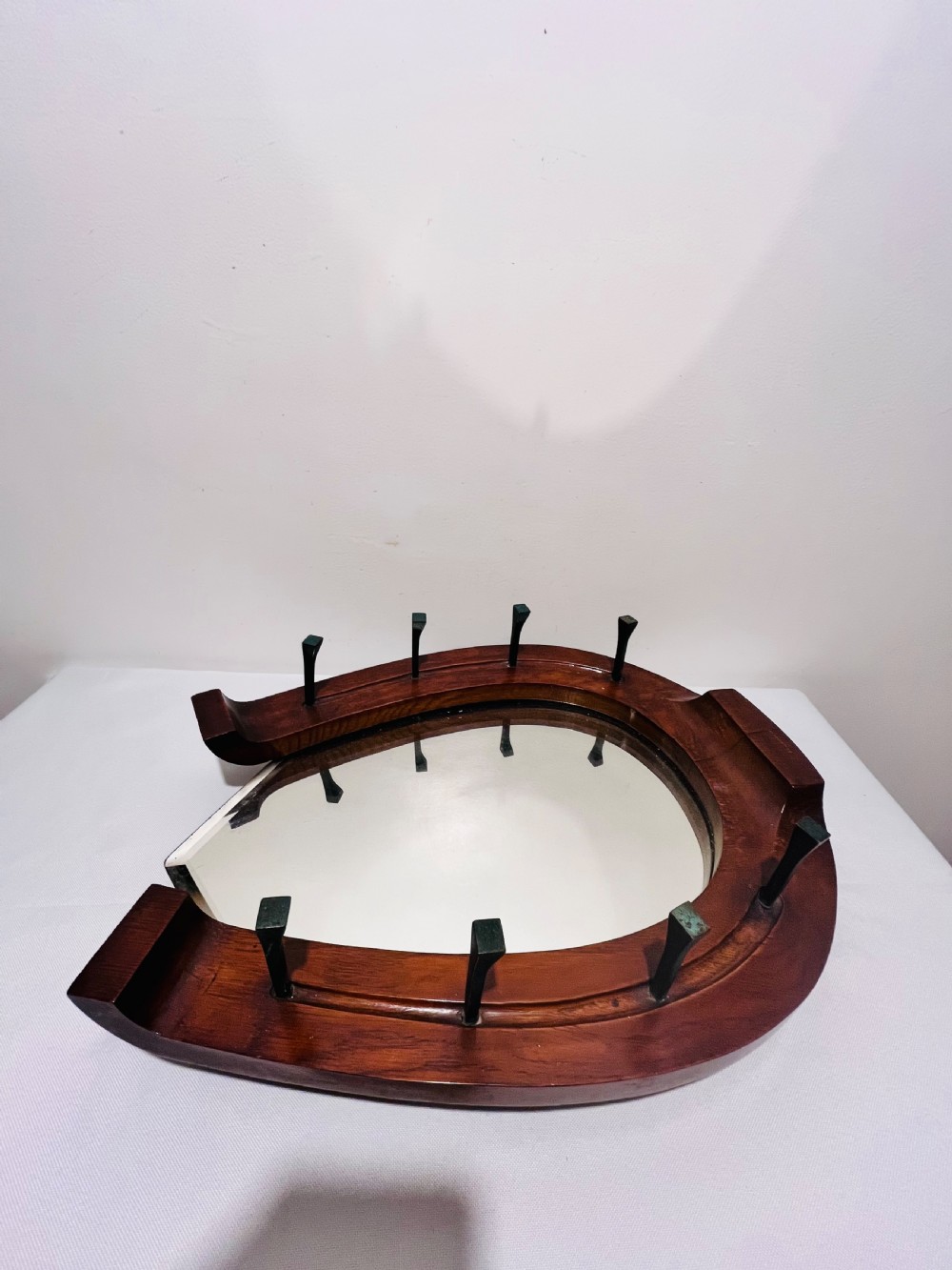 A Victorian horseshoe-shaped wooden wall mirror with bevelled glass and dark metal nail pegs along the frame. View V