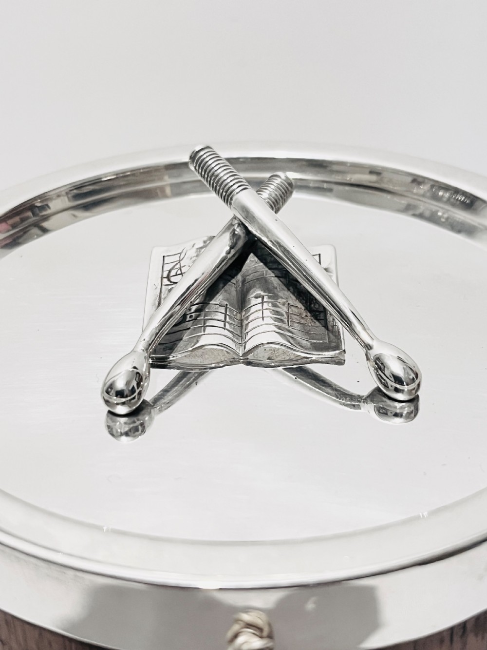 A drum-shaped antique oak biscuit box featuring silver-plated rims, rope cord detail, crossed drumstick lid finial, and a silver swing handle. View V