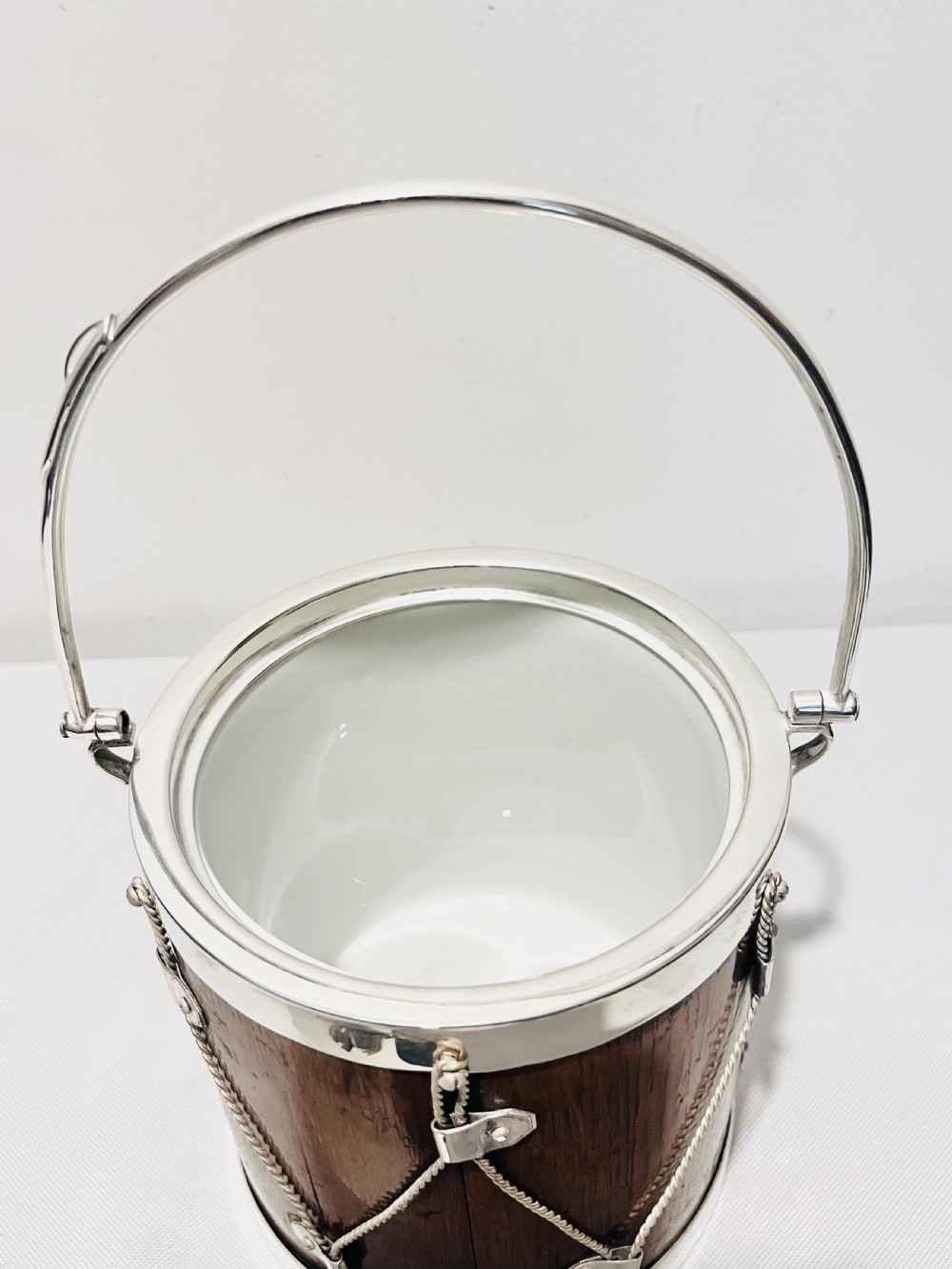 A drum-shaped antique oak biscuit box featuring silver-plated rims, rope cord detail, crossed drumstick lid finial, and a silver swing handle. View VII