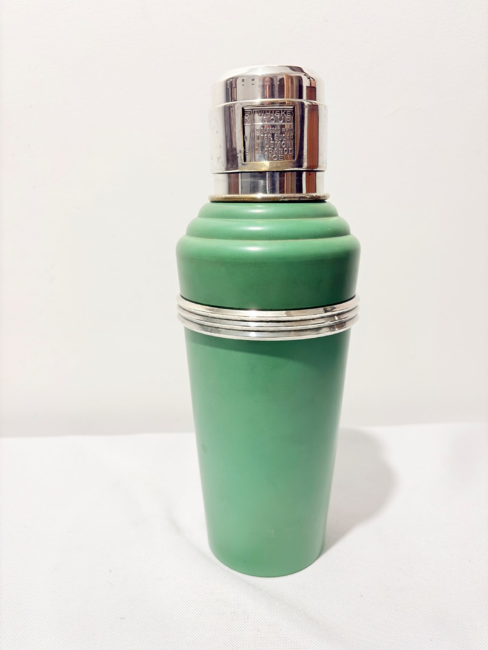 An Art Deco Master Incolor cocktail shaker featuring a green Bakelite body with silver-plated trim and a rotating recipe window cap.