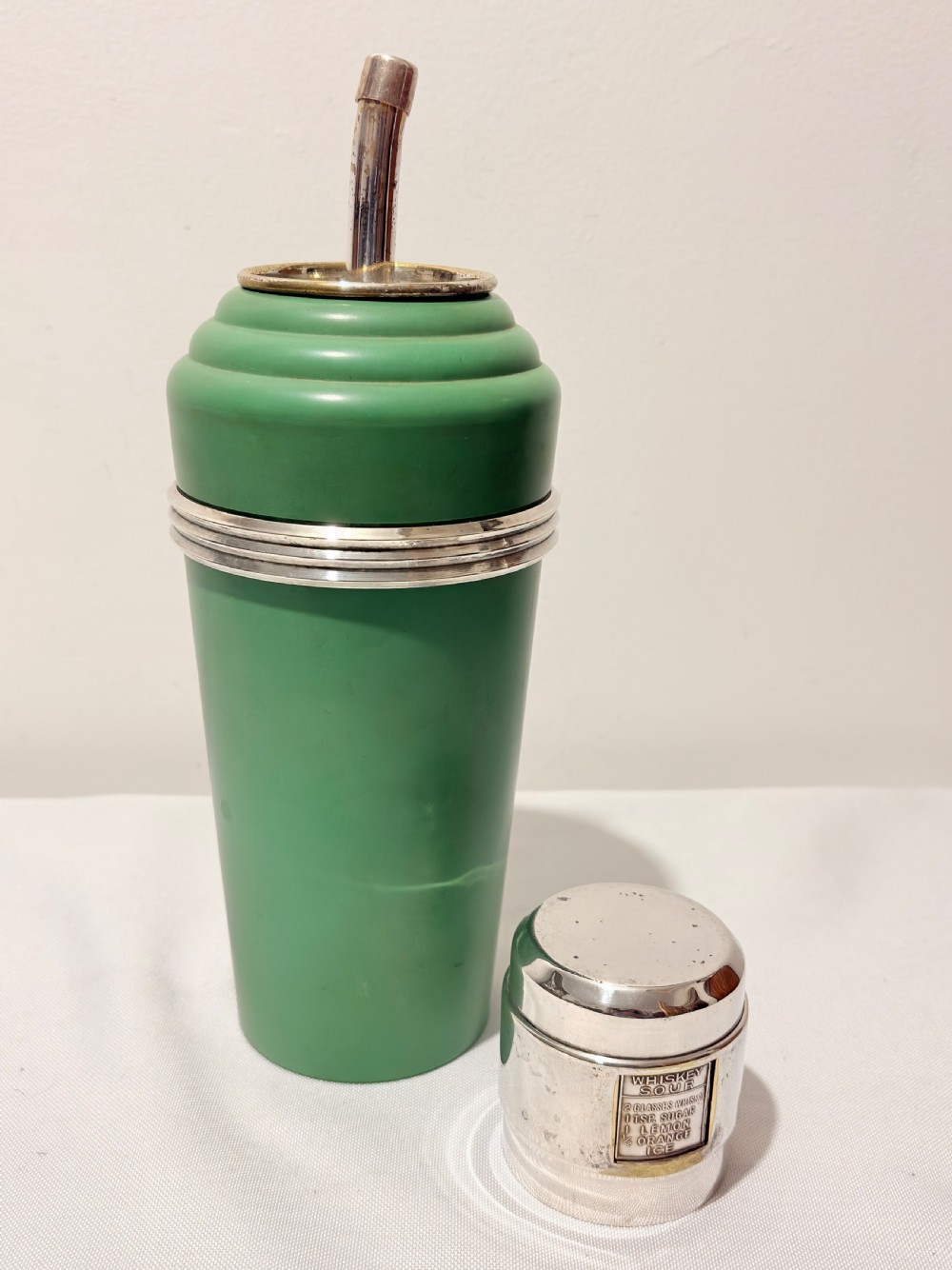 An Art Deco Master Incolor cocktail shaker featuring a green Bakelite body with silver-plated trim and a rotating recipe window cap. View IV