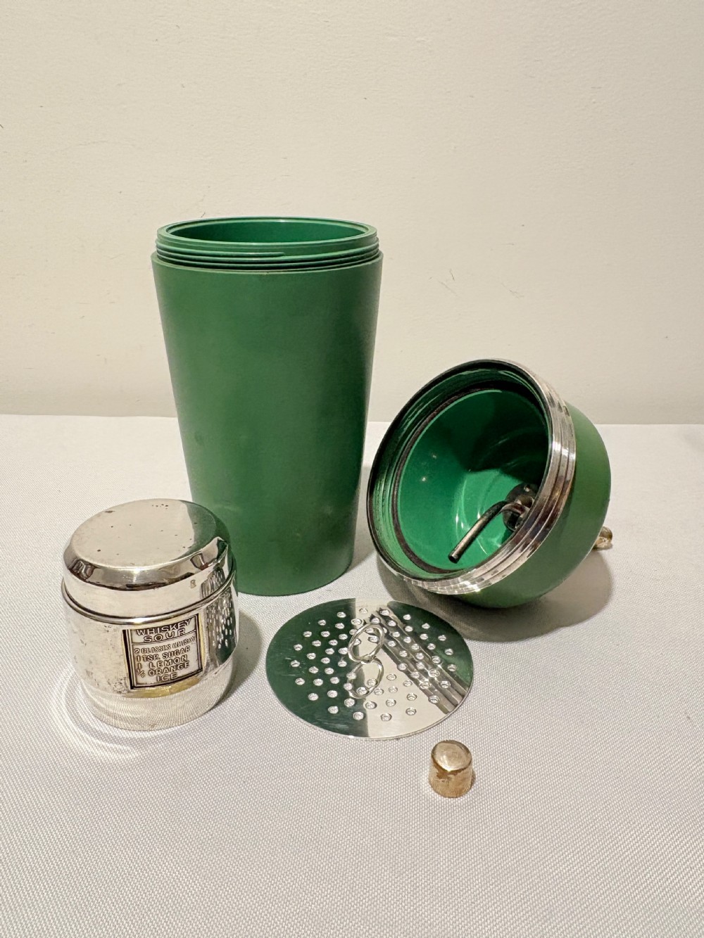 An Art Deco Master Incolor cocktail shaker featuring a green Bakelite body with silver-plated trim and a rotating recipe window cap. View V