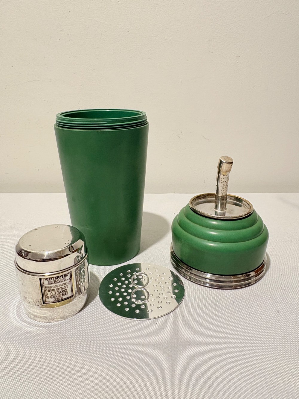 An Art Deco Master Incolor cocktail shaker featuring a green Bakelite body with silver-plated trim and a rotating recipe window cap. View VI