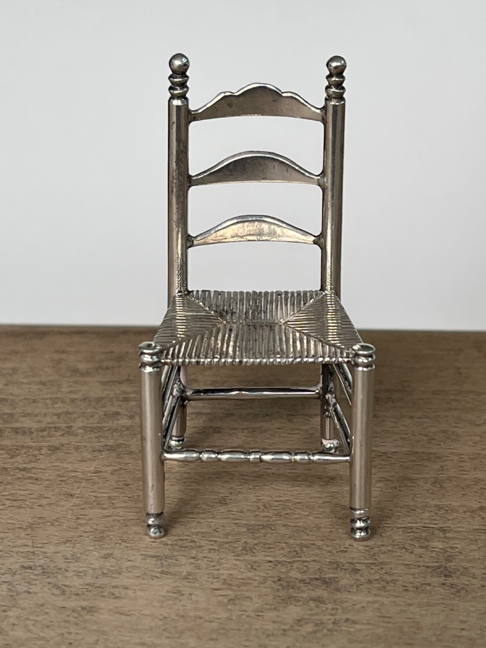 A miniature silver chair featuring a ladderback structure, turned legs topped with finials, and a textured woven seat. View II