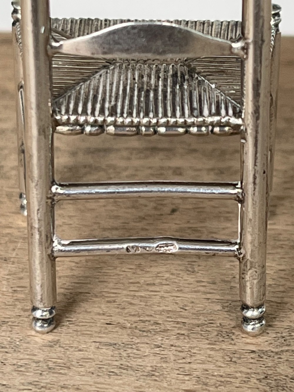 A miniature silver chair featuring a ladderback structure, turned legs topped with finials, and a textured woven seat. View VII