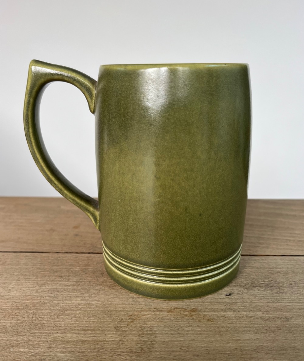 A green glazed Art Deco ceramic tankard featuring a geometric angular handle and subtle concentric ribbed detail around the base.