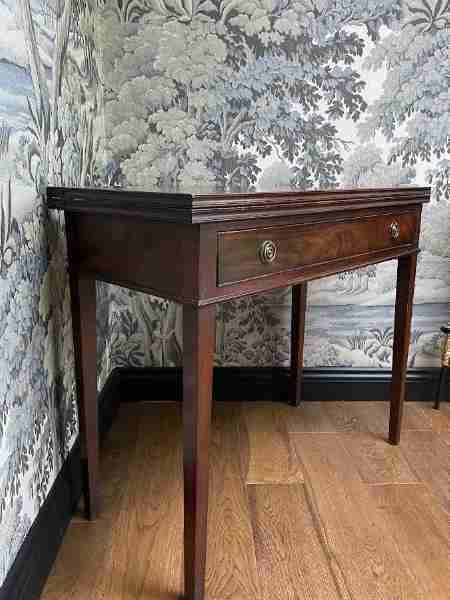 fig 1. A 19th-century mahogany fold-over tea table featuring a rectangular top, frieze drawer with brass ring handles, and four square tapered legs.