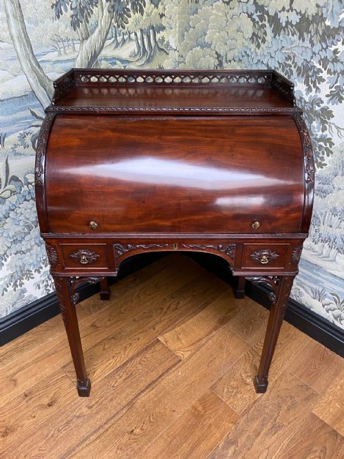 fig 1. A dark mahogany Georgian cylinder desk featuring a curved roll-top hood, carved corner brackets, small drawers, and a pierced fretwork gallery top.
