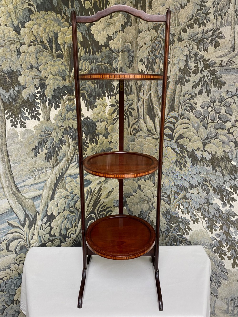 An Edwardian mahogany folding cake stand featuring three circular inlaid tiers connected by slender uprights and splayed feet.