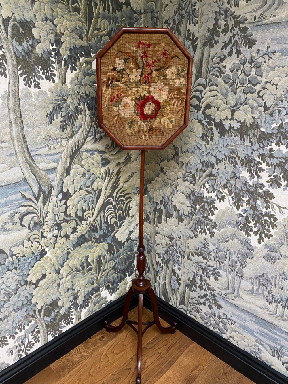 An antique mahogany pole screen featuring an octagonal framed floral needlepoint panel supported by an adjustable slender stem and tripod base.
