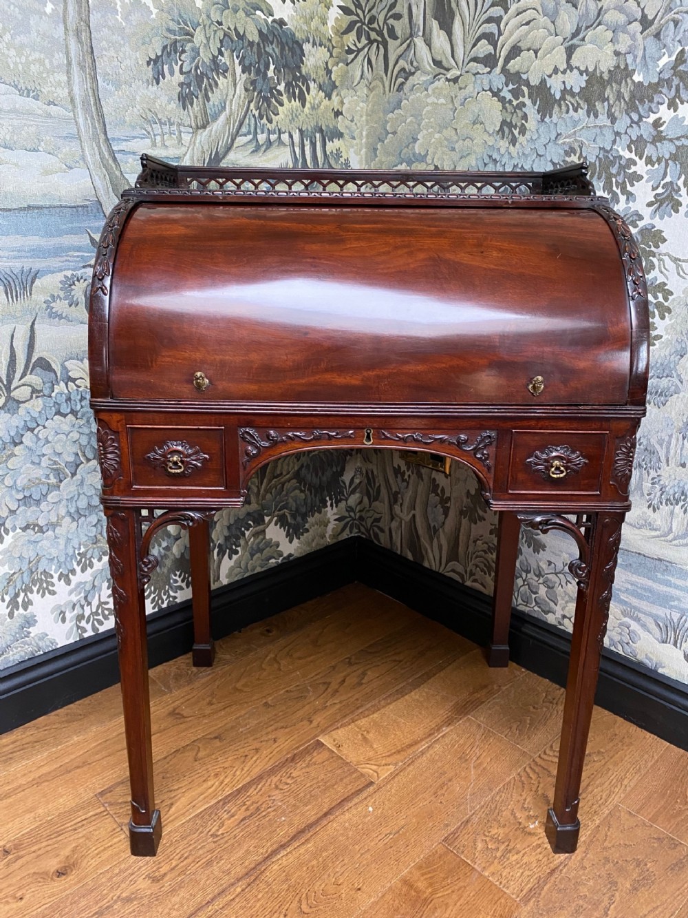 A dark mahogany Georgian cylinder desk featuring a curved roll-top hood, carved corner brackets, small drawers, and a pierced fretwork gallery top.