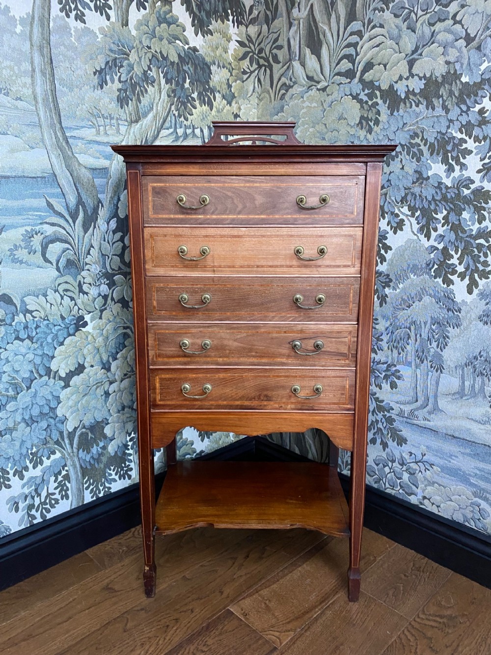 A tall Edwardian mahogany music cabinet featuring five drop-front drawers with brass handles, boxwood line inlay, an open bottom shelf, and a top gallery rail.