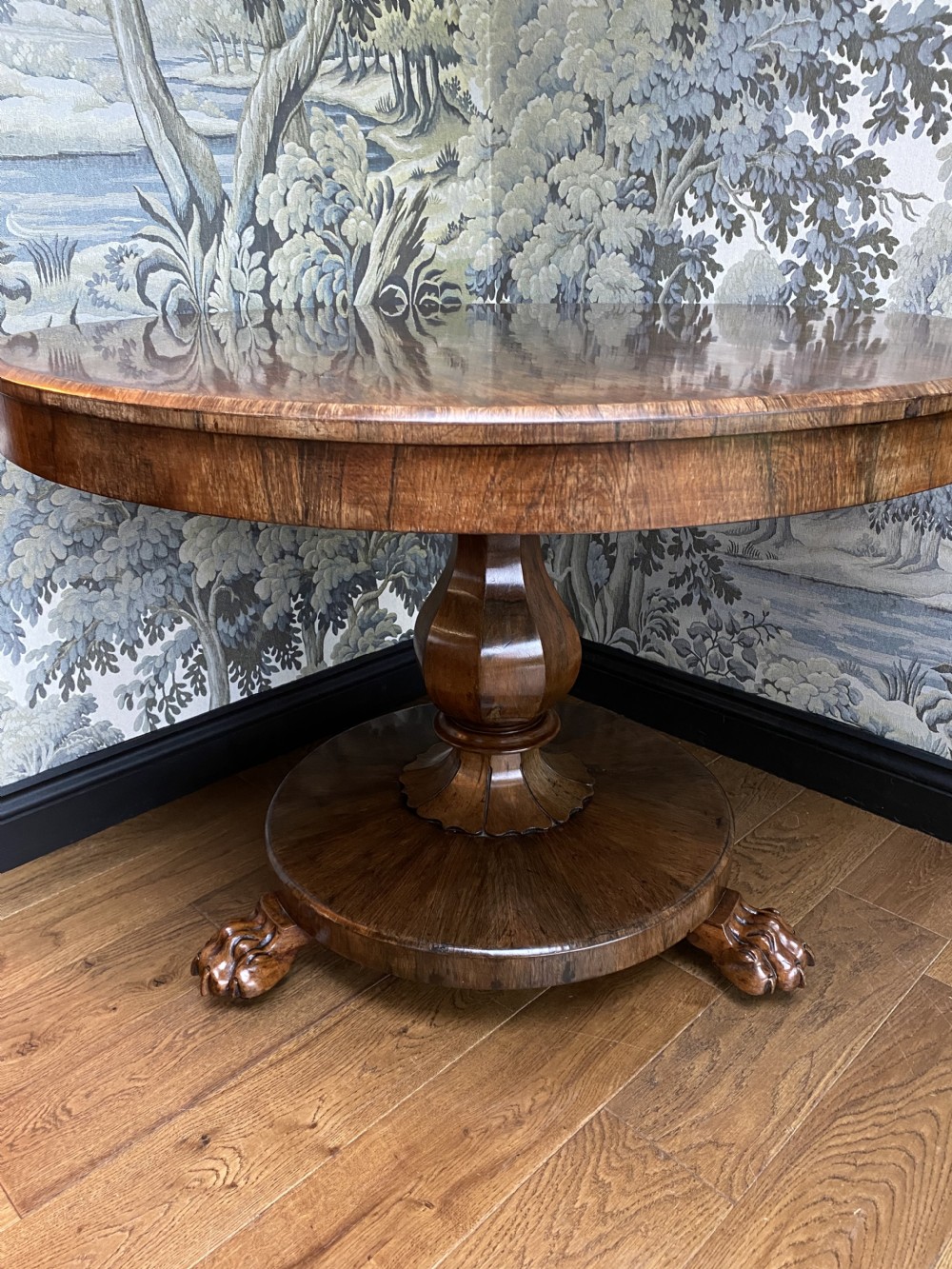 A circular dark wood tilt-top table featuring a polished figured grain, raised on a central pedestal column with carved lion paw feet. View IV