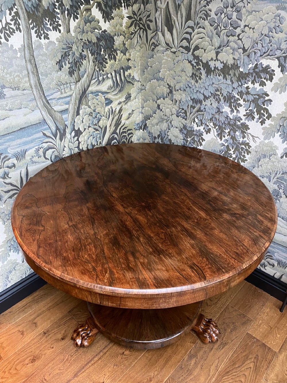 A circular dark wood tilt-top table featuring a polished figured grain, raised on a central pedestal column with carved lion paw feet.