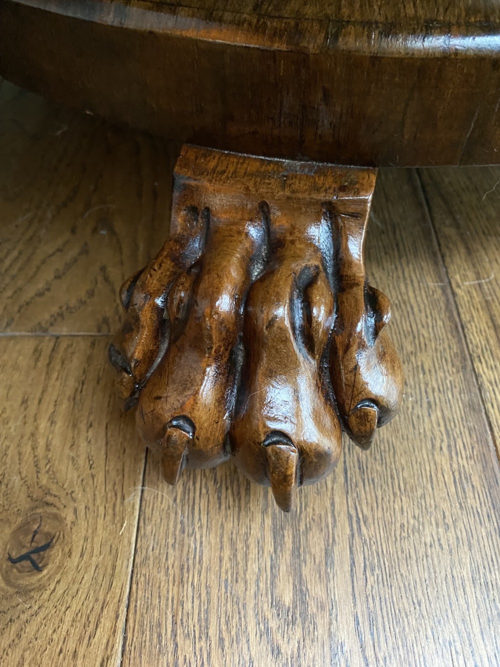 A circular dark wood tilt-top table featuring a polished figured grain, raised on a central pedestal column with carved lion paw feet. View II