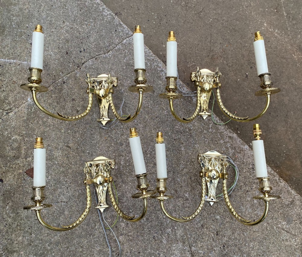 Set of four Edwardian cast brass twin-arm wall lights with reeded scroll arms, foliate backplates, and cream candle sleeves. View II