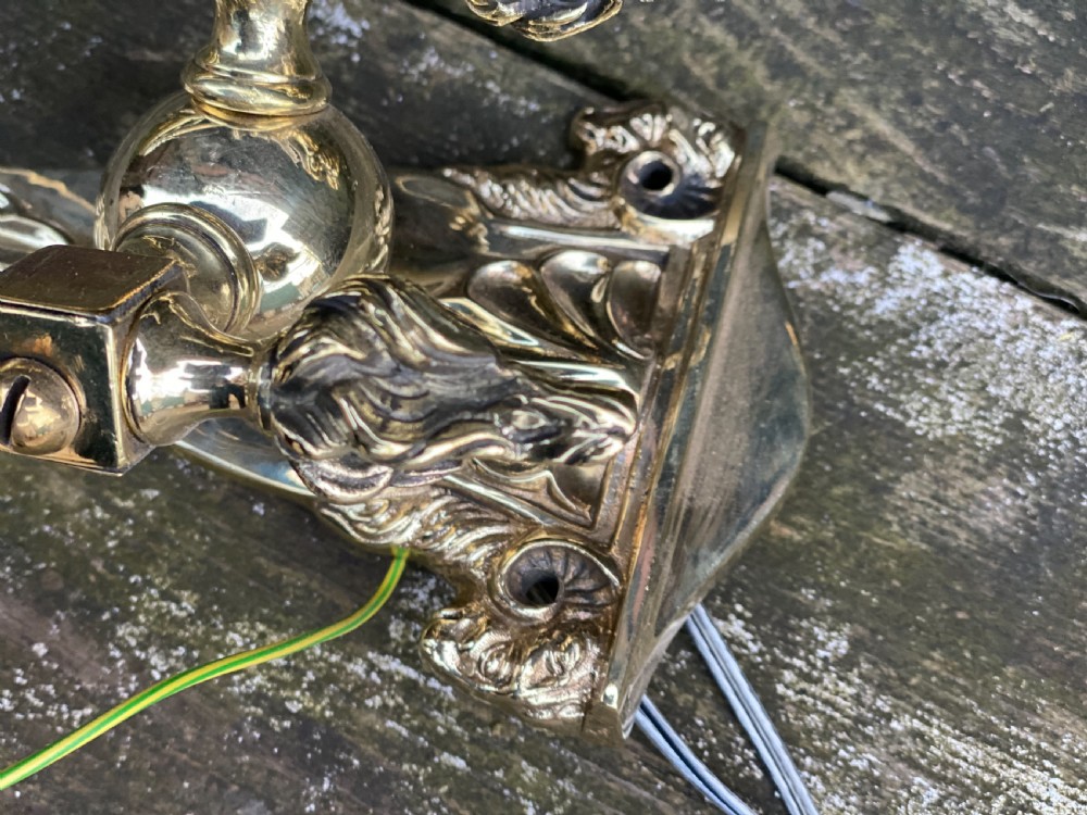 Set of four Edwardian cast brass twin-arm wall lights with reeded scroll arms, foliate backplates, and cream candle sleeves. View IV