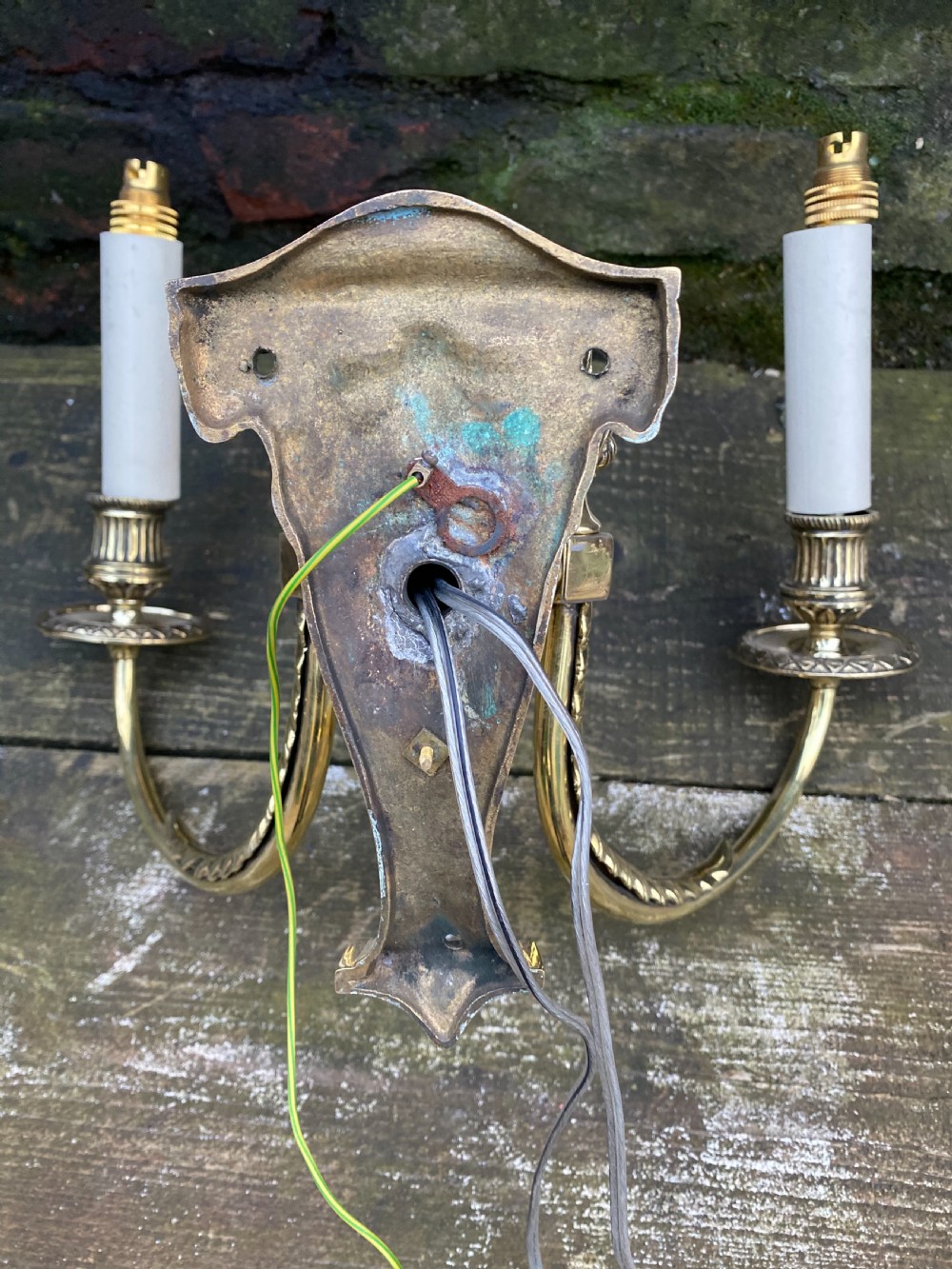 Set of four Edwardian cast brass twin-arm wall lights with reeded scroll arms, foliate backplates, and cream candle sleeves. View V