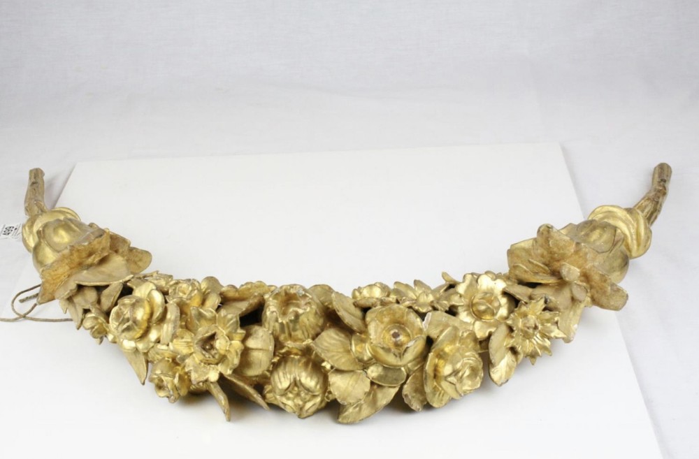 An 18th-century carved wood floral swag featuring detailed blossom carvings with a distressed gold leaf finish.