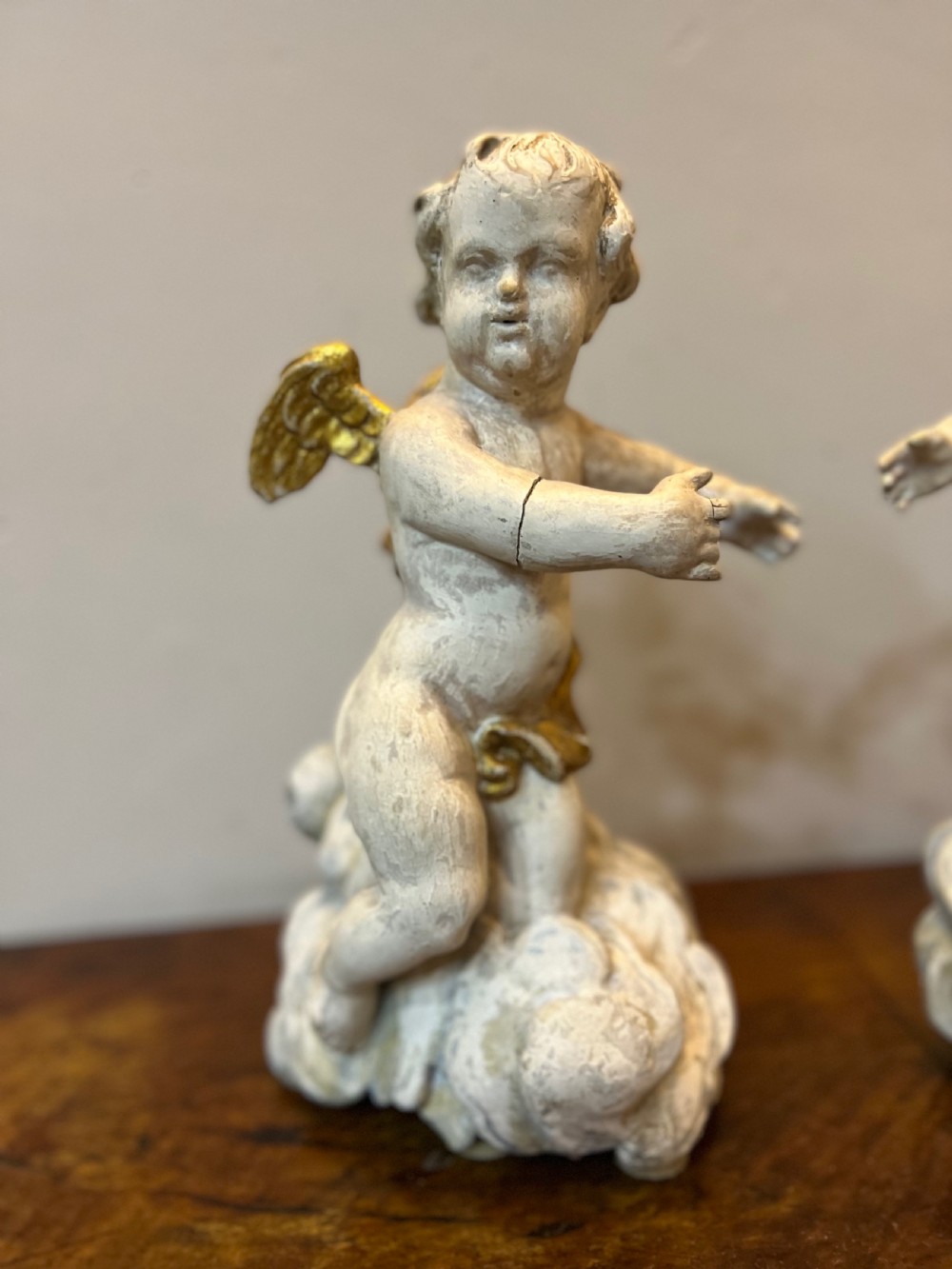 A pair of 18th-century carved wood polychrome putti featuring painted off-white figures with gilded wings and drapery, resting upon carved cloud bases. View II