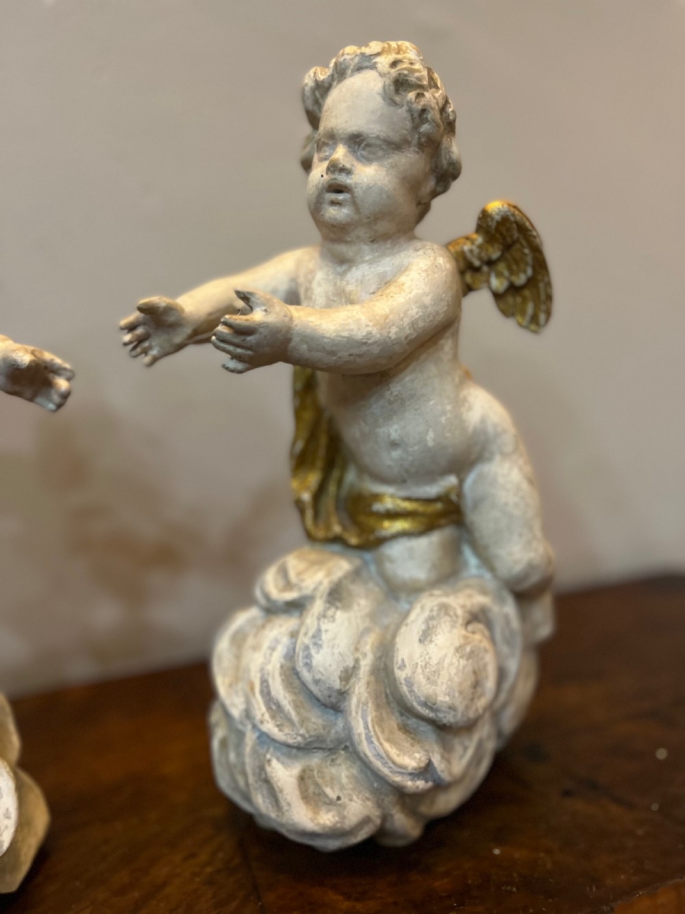 A pair of 18th-century carved wood polychrome putti featuring painted off-white figures with gilded wings and drapery, resting upon carved cloud bases. View III