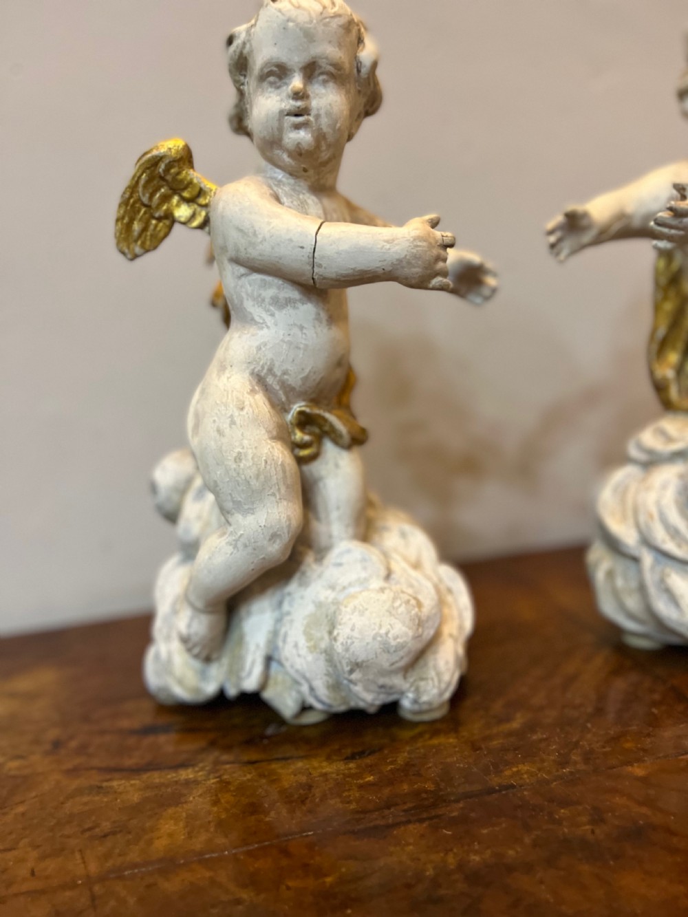 A pair of 18th-century carved wood polychrome putti featuring painted off-white figures with gilded wings and drapery, resting upon carved cloud bases. View VII