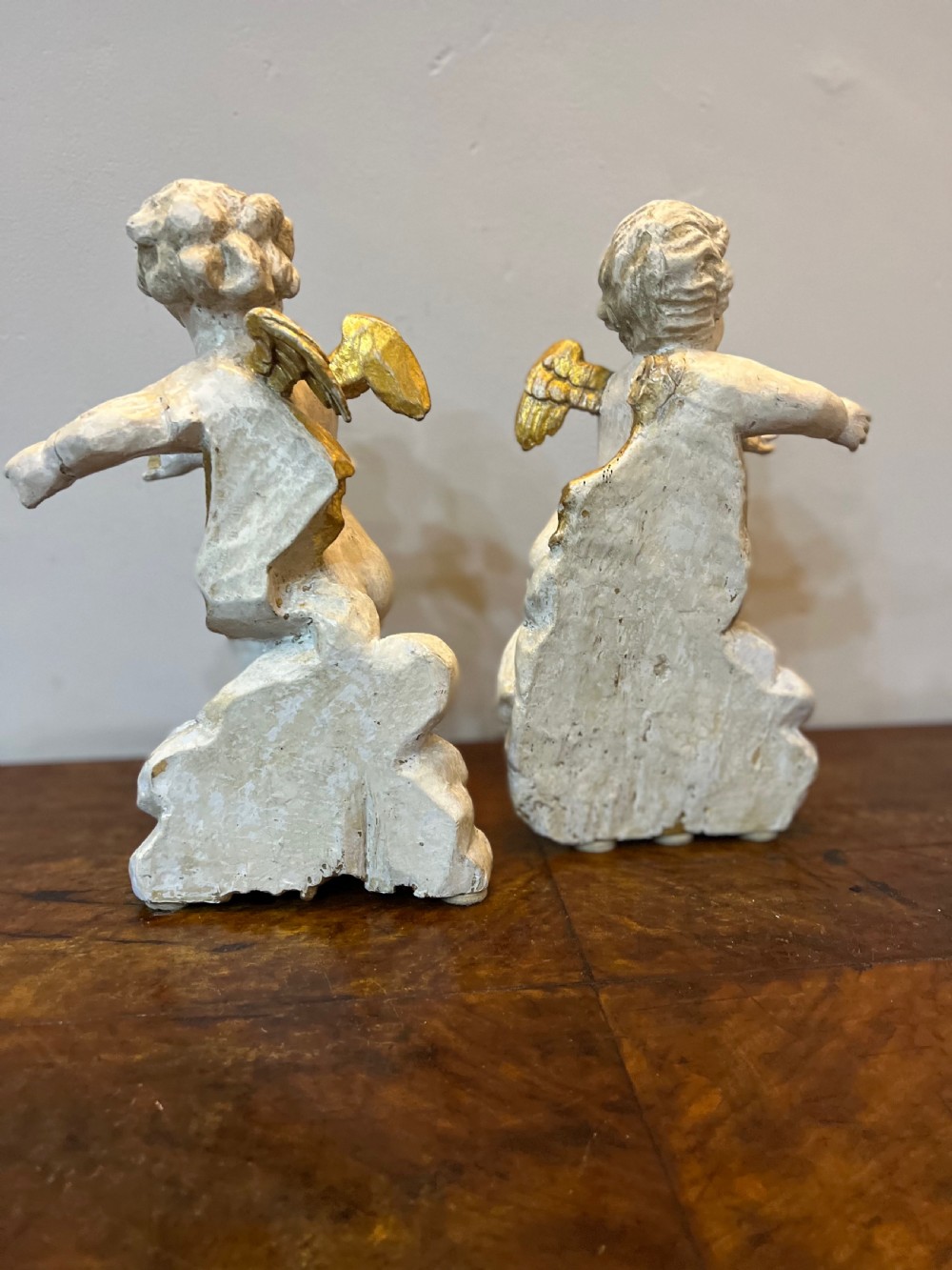 A pair of 18th-century carved wood polychrome putti featuring painted off-white figures with gilded wings and drapery, resting upon carved cloud bases. View VIII