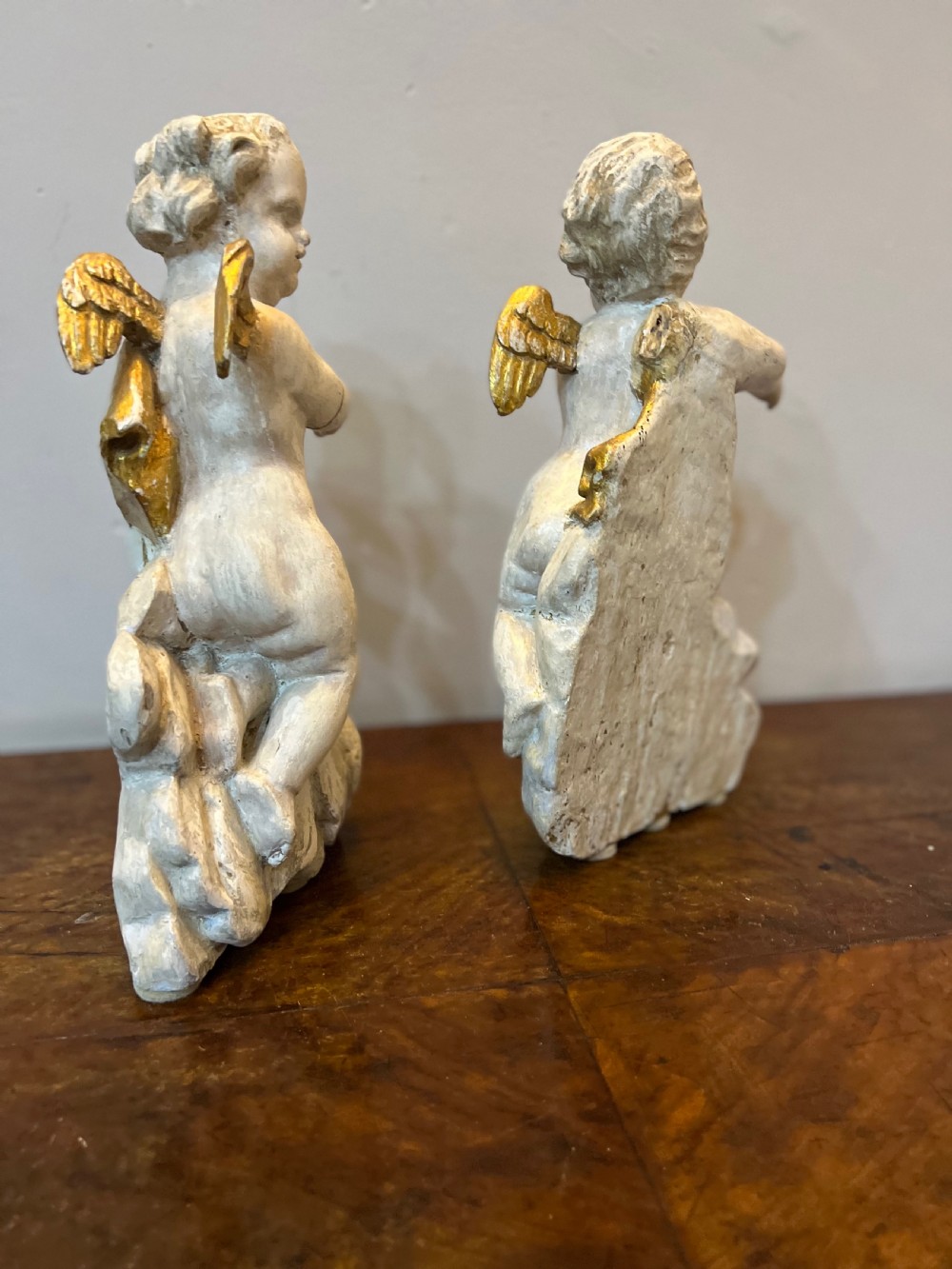 A pair of 18th-century carved wood polychrome putti featuring painted off-white figures with gilded wings and drapery, resting upon carved cloud bases. View IX